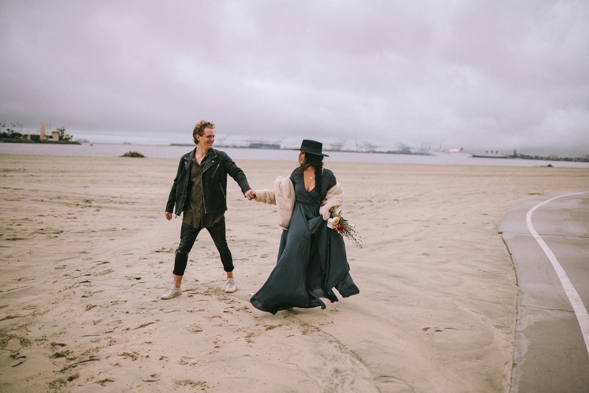 A couple holding hands and walking on a beach in cloudy weather, sharing a romantic moment.