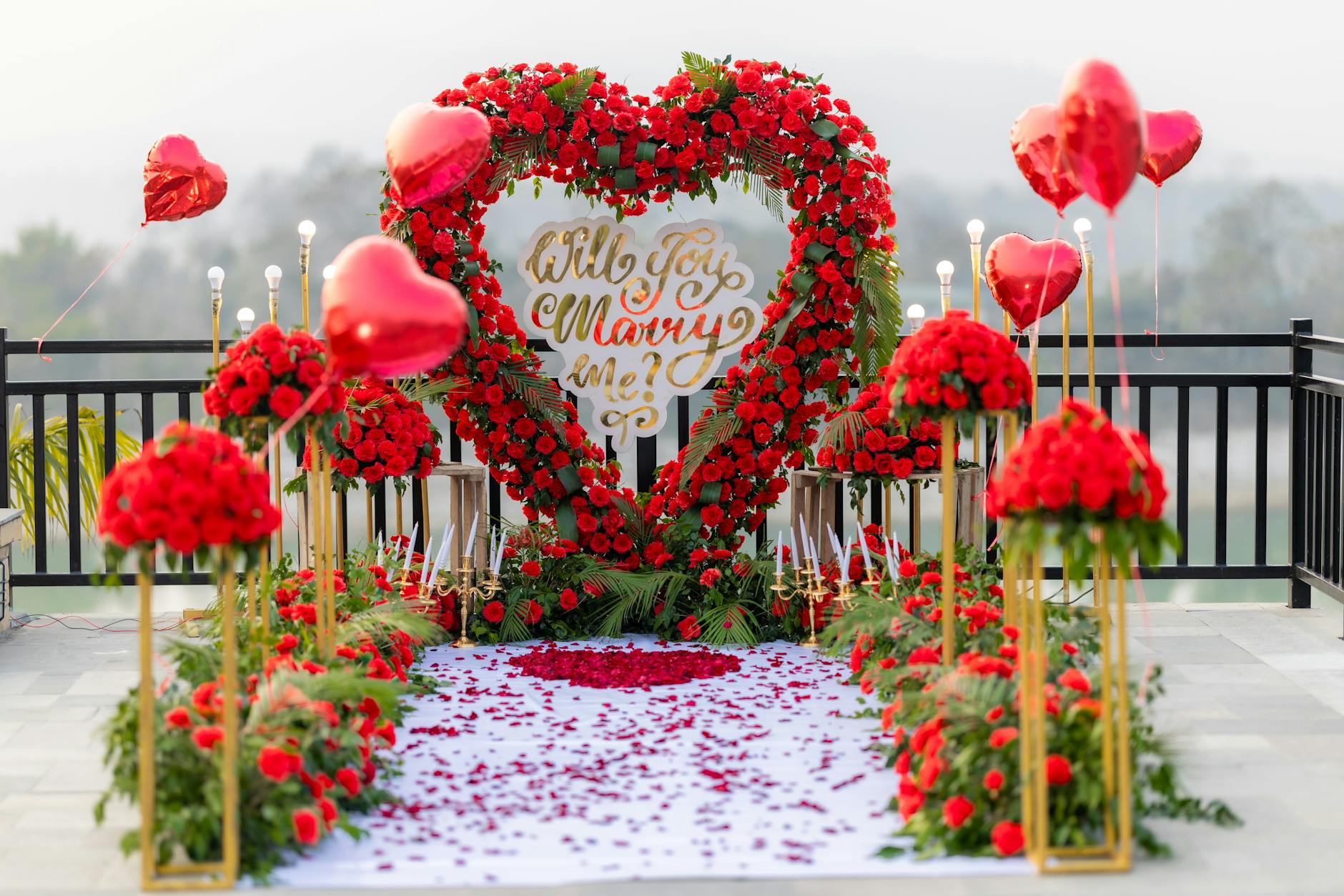 A romantic outdoor marriage proposal setup with heart-shaped roses and red balloons.