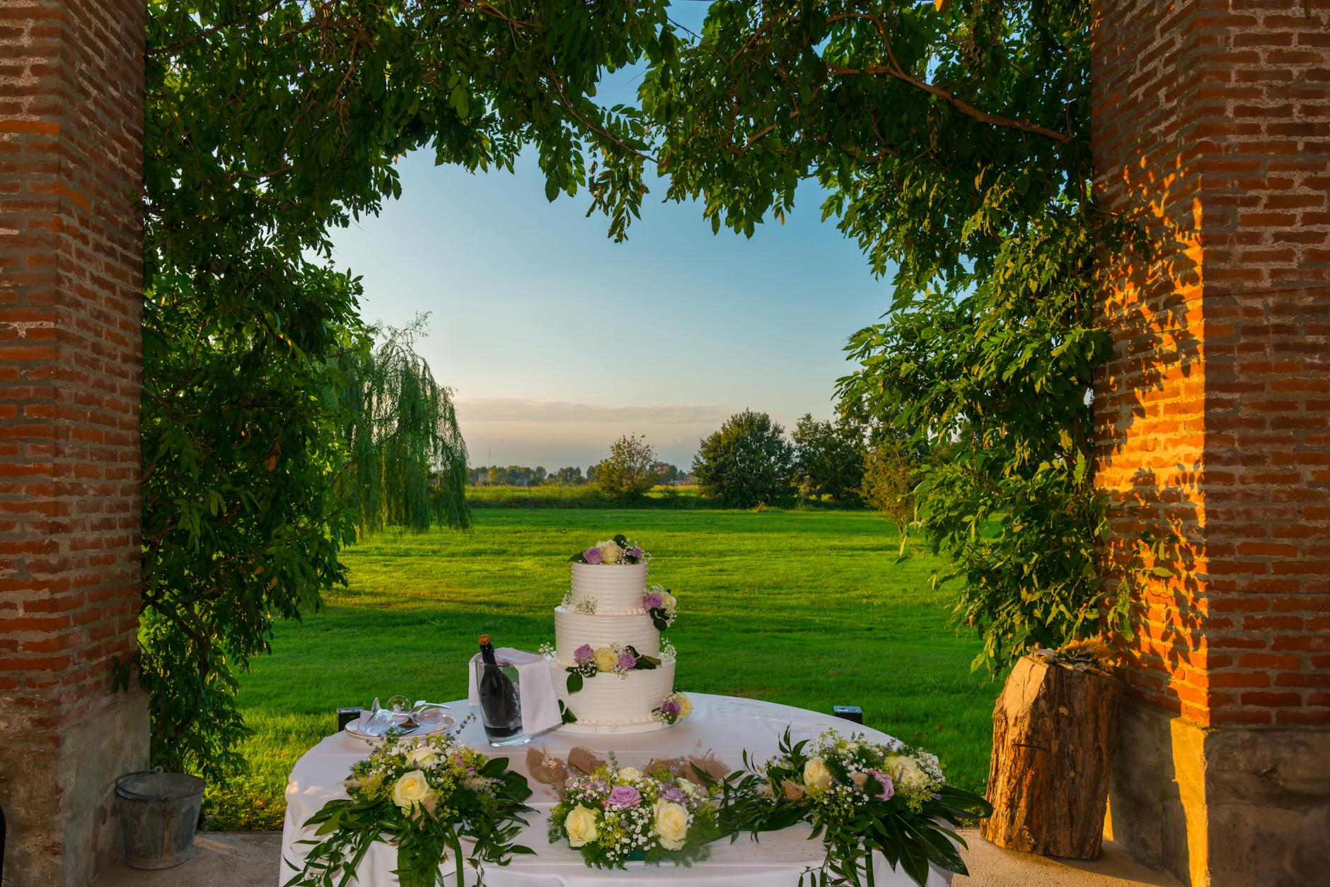 A beautifully decorated wedding cake table outdoors with lush greenery and brick walls, capturing a serene setting.