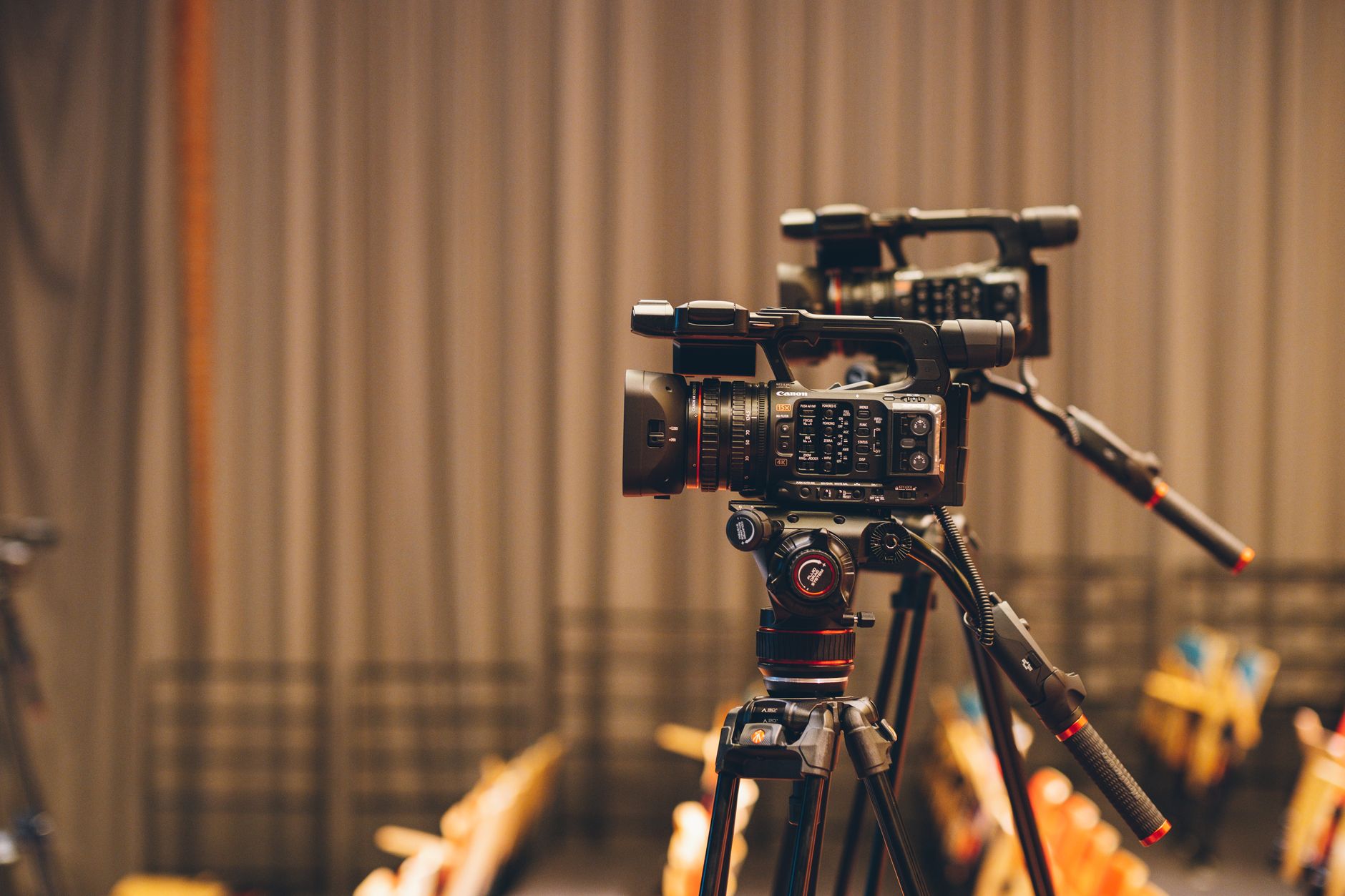 Close-up of professional video cameras on tripods, set up indoors for filming.