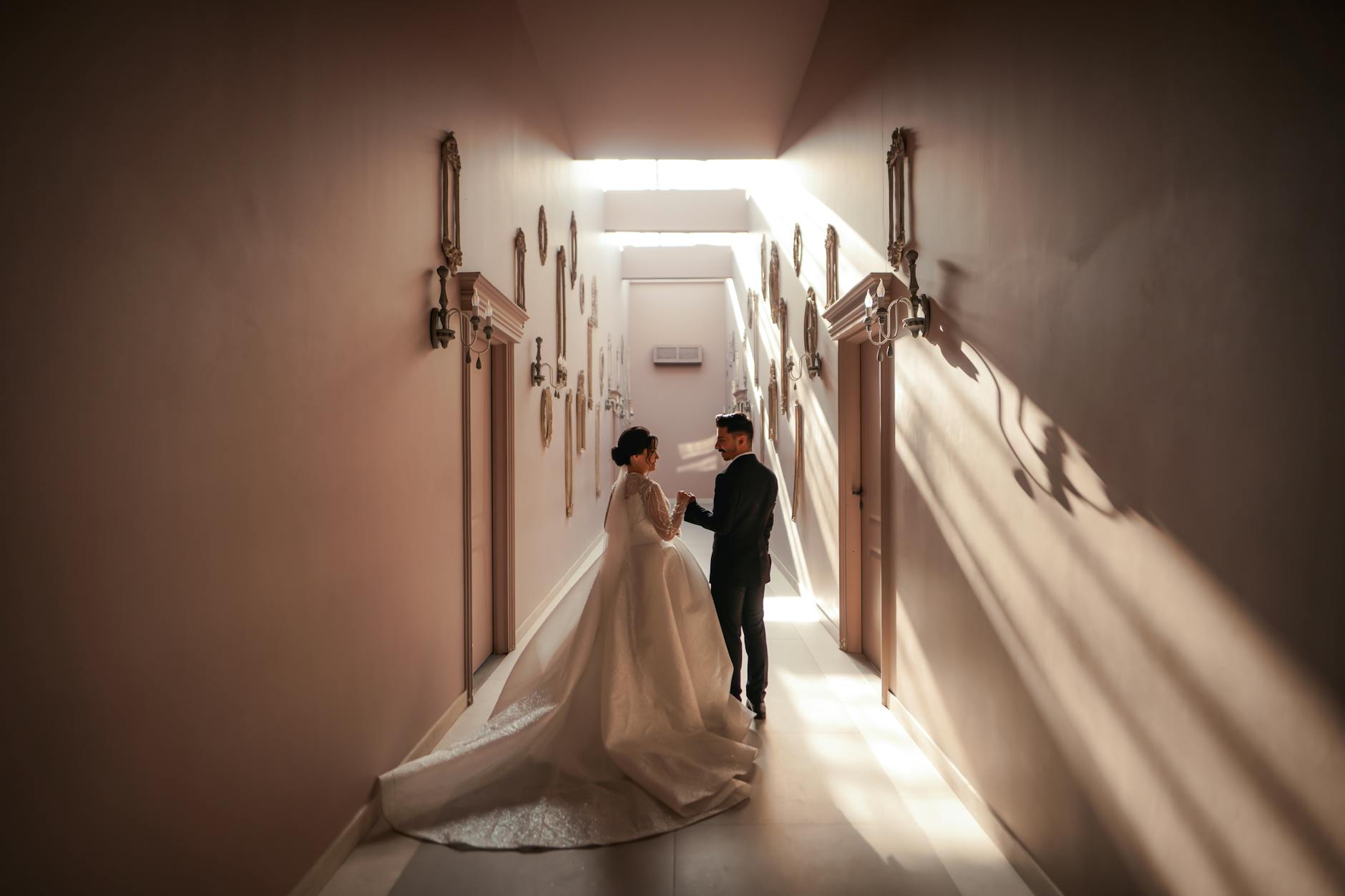 A bride and groom share a moment in a beautifully lit corridor, highlighting their wedding attire.