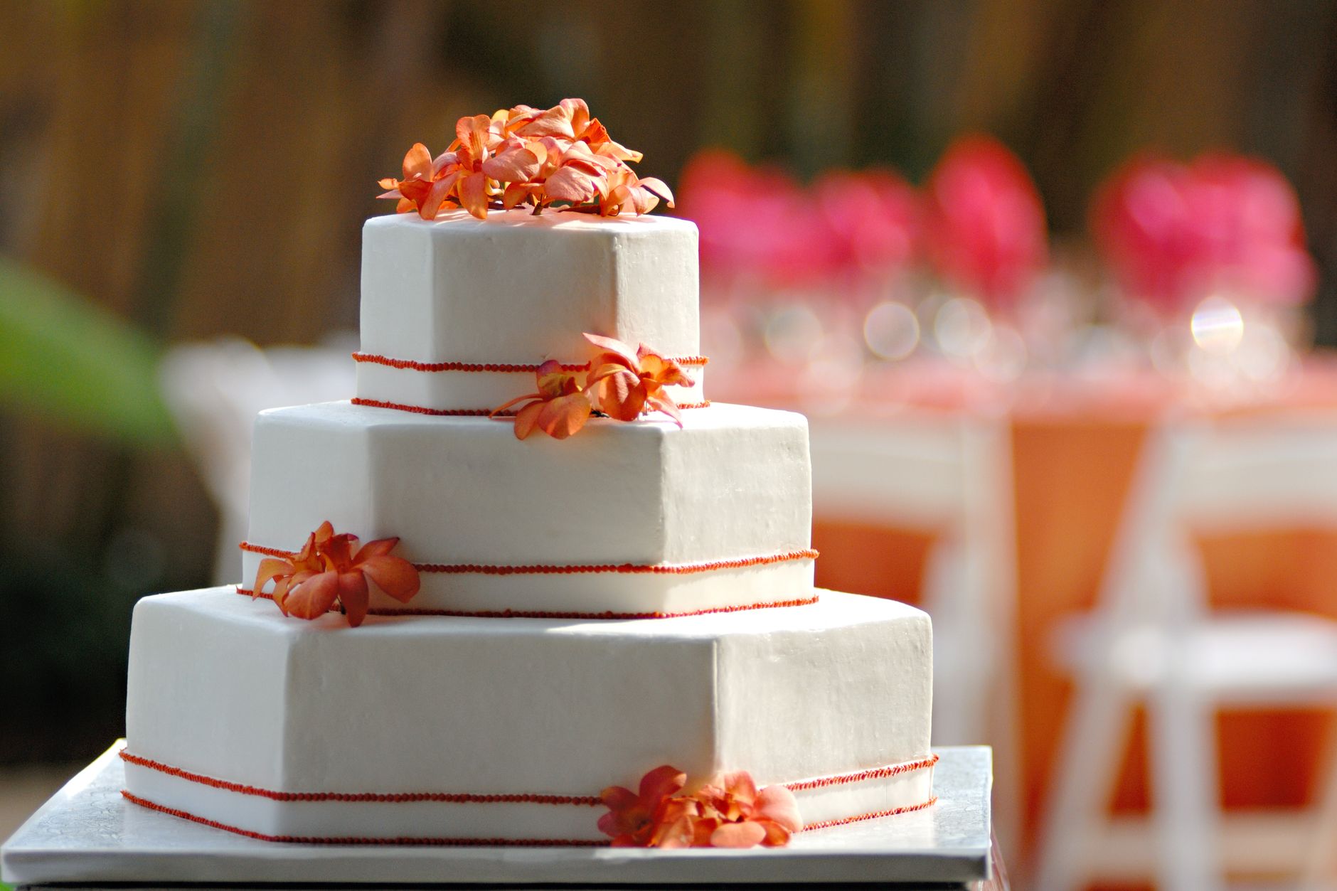 Three-tier wedding cake adorned with orange flowers, perfect for a stylish outdoor celebration.